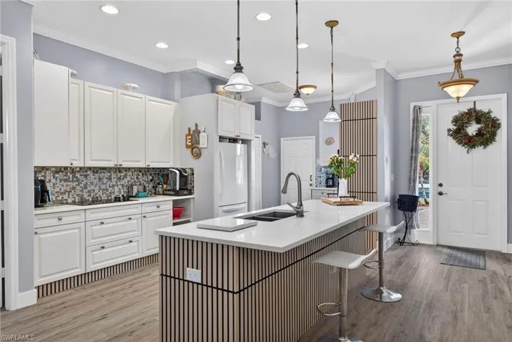 Kitchen with a kitchen breakfast bar, crown molding, white cabinetry, light wood finished floors, and pendant lighting