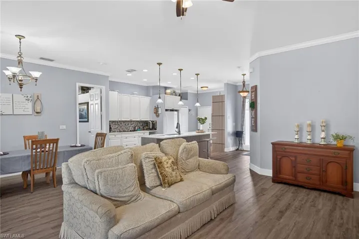 Living room featuring ornamental molding, hanging lights, dark wood-style floors, and ceiling fan