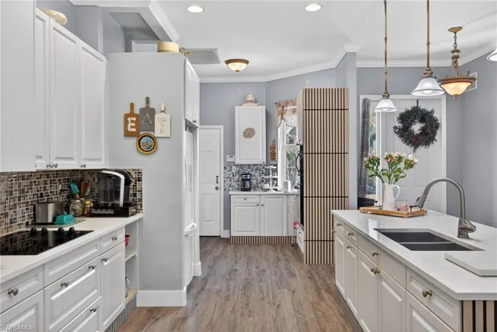 Kitchen with backsplash, white cabinets, crown molding, pendant lighting, and black electric stovetop