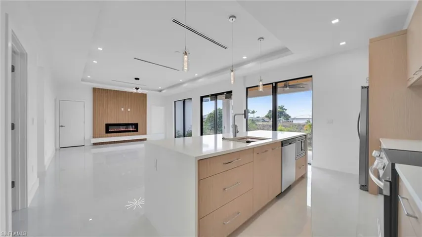 Kitchen featuring light brown cabinetry, hanging light fixtures, open floor plan, a tray ceiling, and recessed lighting
