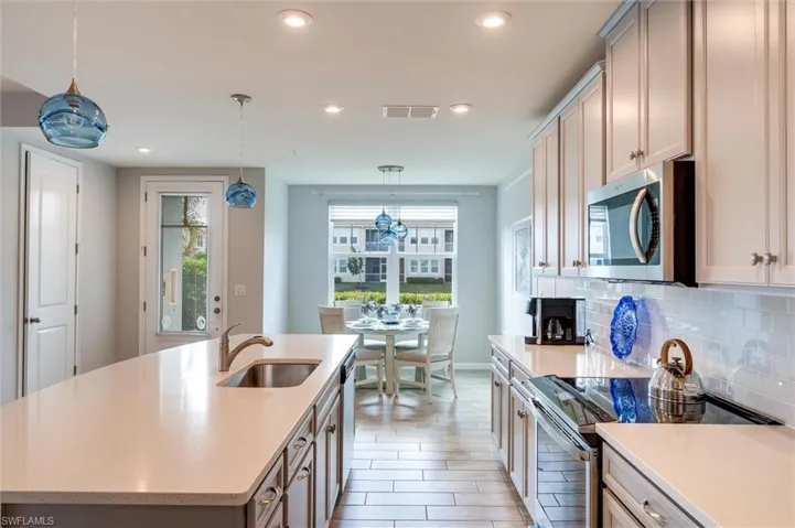 Kitchen with stainless steel appliances, decorative light fixtures, a kitchen island with sink, light stone counters, and recessed lighting