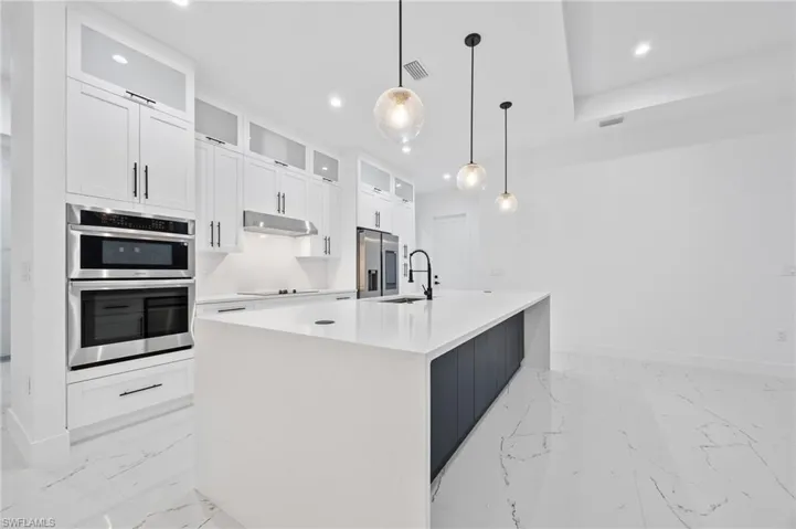Kitchen featuring glass insert cabinets, white cabinets, pendant lighting, stainless steel appliances, and a kitchen island with sink