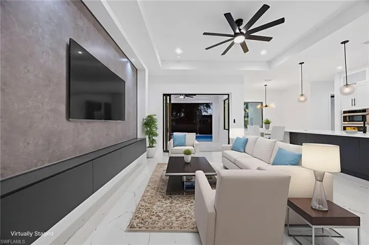 Living area with ceiling fan, light marble finish floors, recessed lighting, a tray ceiling, and a chandelier
