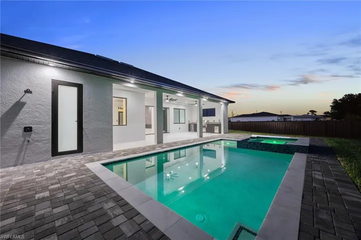 Pool at dusk with a patio area, a fenced backyard, and a pool with connected hot tub