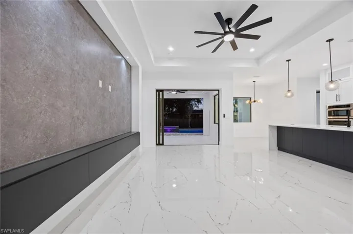 Unfurnished living room featuring a ceiling fan, a chandelier, light marble finish floors, a tray ceiling, and recessed lighting