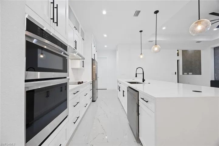 Kitchen featuring stainless steel appliances, recessed lighting, white cabinets, light stone countertops, and pendant lighting