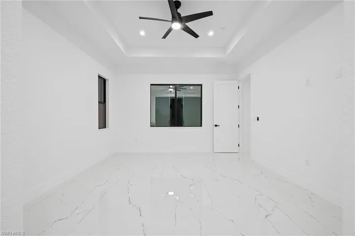 Empty room with a ceiling fan, a raised ceiling, light marble finish flooring, and recessed lighting