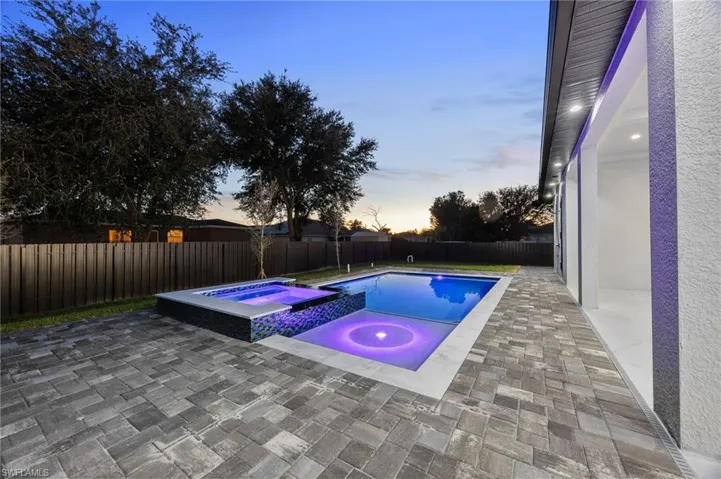 Pool at dusk featuring a patio area, a fenced backyard, and a pool with connected hot tub