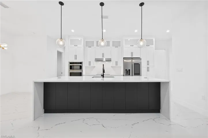 Kitchen featuring glass insert cabinets, a large island with sink, white cabinets, stainless steel appliances, and decorative light fixtures