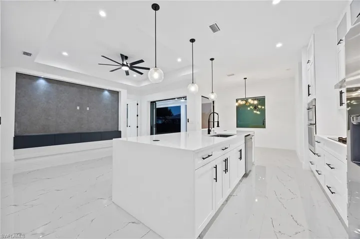 Kitchen featuring white cabinets, light stone counters, a tray ceiling, decorative light fixtures, and recessed lighting