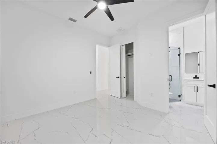Unfurnished bedroom featuring light marble finish flooring, ceiling fan, connected bathroom, and a closet