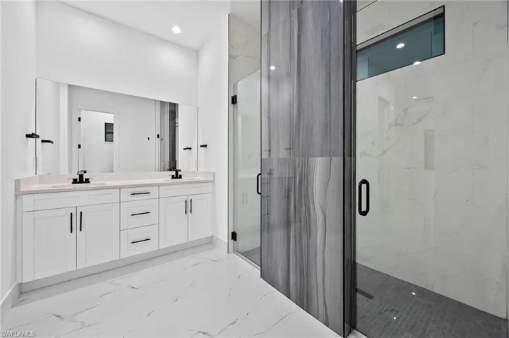 Bathroom featuring double vanity, a marble finish shower, light marble finish floors, and recessed lighting