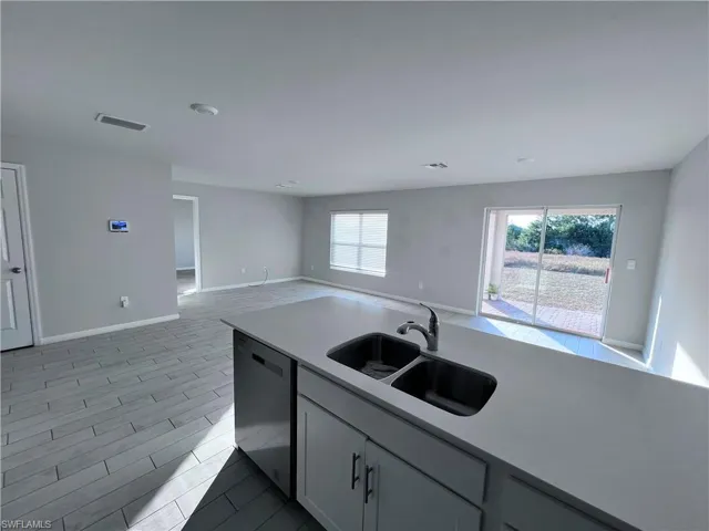 Kitchen with dishwasher, open floor plan, light stone countertops, and wood finish floors