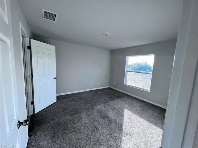 Spare room featuring dark colored carpet and baseboards