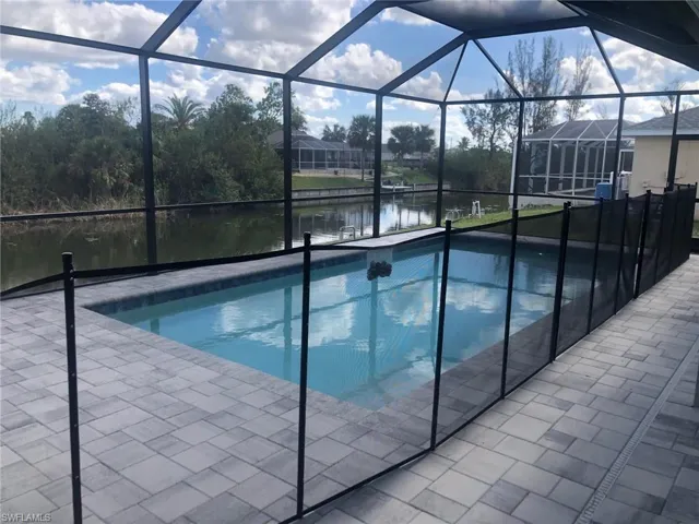 View of pool featuring glass enclosure, a patio area, and a water view