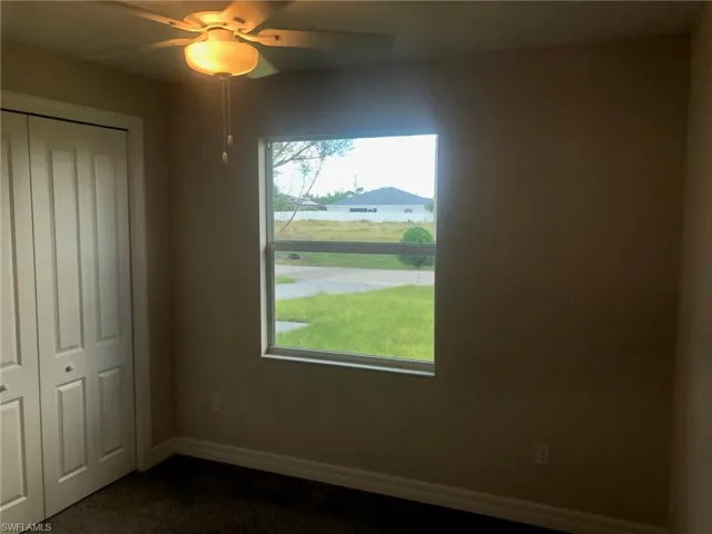 Unfurnished bedroom with multiple windows, ceiling fan, dark carpet, and a closet