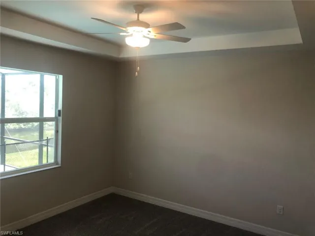 Empty room featuring carpet, ceiling fan, and a tray ceiling