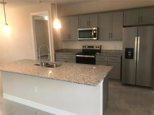 Kitchen with stainless steel appliances, sink, light stone counters, hanging light fixtures, and decorative backsplash