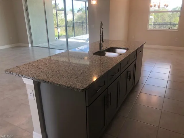 Kitchen with a kitchen island with sink, dishwasher, sink, and light stone counters