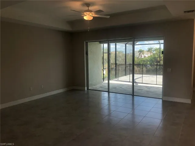 Unfurnished room featuring a tray ceiling, tile patterned flooring, and ceiling fan