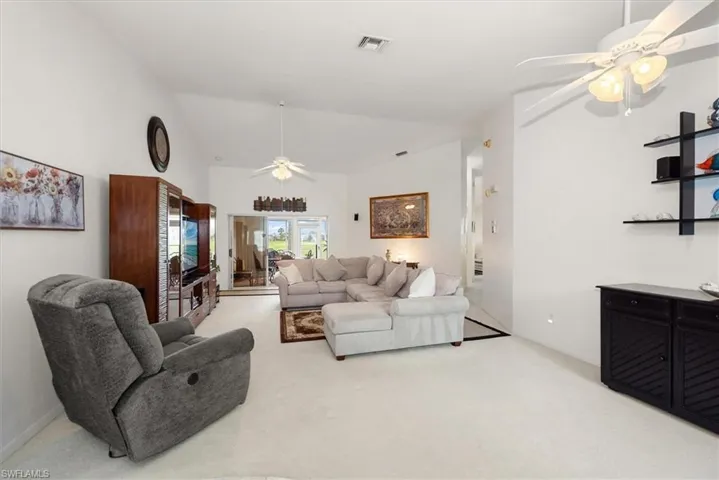 Spacious living area featuring vaulted ceilings, light-toned carpeting, and a built-in media console with glass paneling