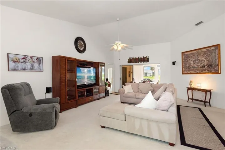 Spacious living area featuring vaulted ceilings, a ceiling fan, and light-toned carpet flooring