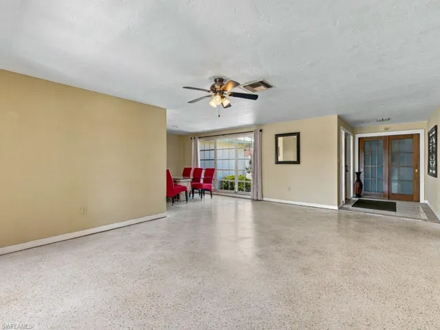 Expansive living area featuring terrazzo flooring, a ceiling fan with integrated lighting, large windows, and double entry doors with glass inserts
