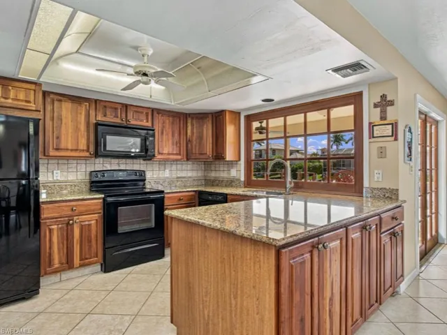 Kitchen featuring wood cabinetry, stone countertops, a center island with sink, a built-in microwave, and tile flooring