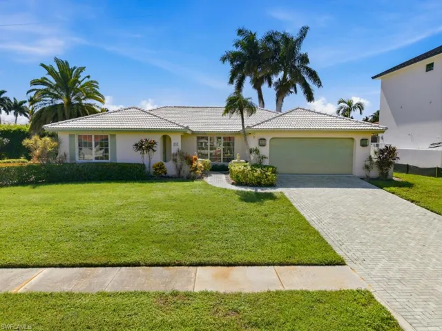 Single-story residence featuring a tile roof, paved driveway, arched entryway, and mature palm trees