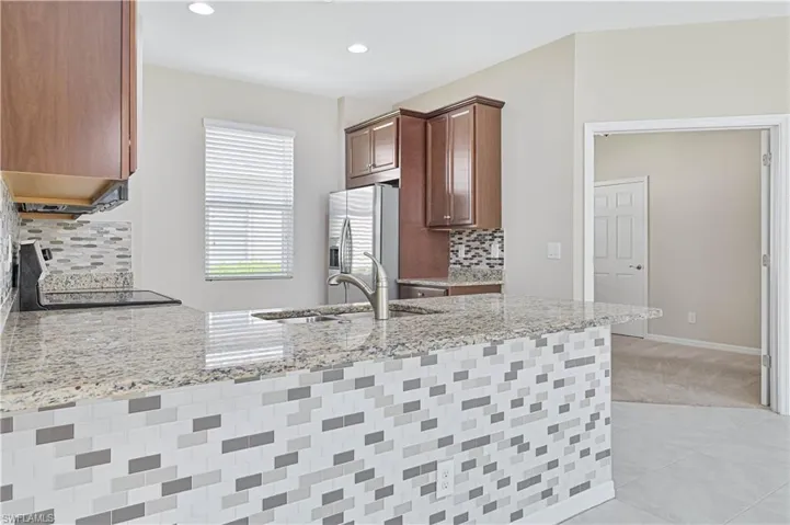 Kitchen with backsplash, light stone countertops, a peninsula, stainless steel fridge, and light tile patterned floors