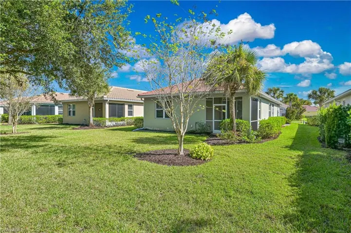 Back of property featuring a lawn, a sunroom, stucco siding, and a tiled roof