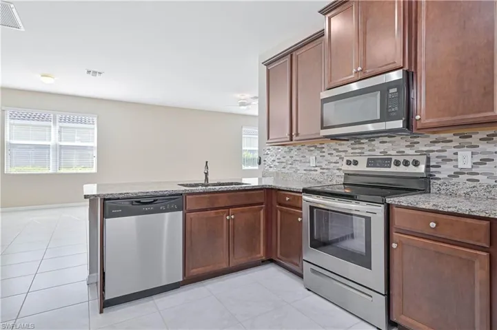 Kitchen featuring stainless steel appliances, a peninsula, light tile patterned floors, backsplash, and light stone counters