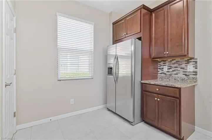 Kitchen with stainless steel fridge with ice dispenser, backsplash, light stone countertops, light tile patterned floors, and plenty of natural light