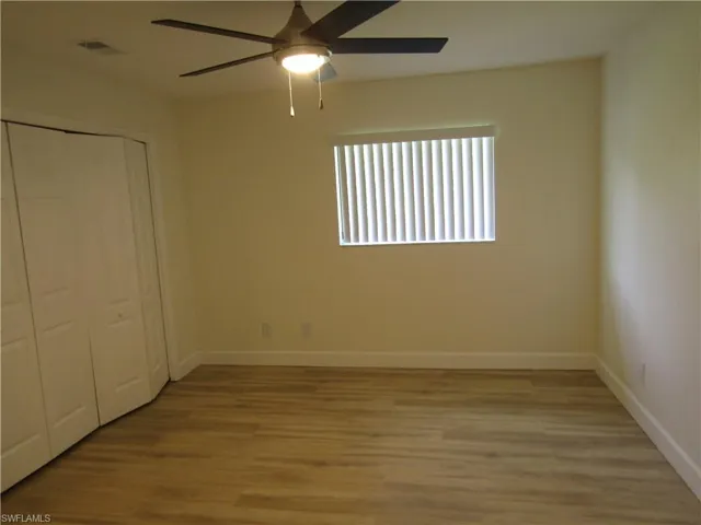 Neutral-toned room featuring wood-finish flooring, a ceiling fan with integrated lighting, a window with horizontal blinds, and bi-fold closet doors