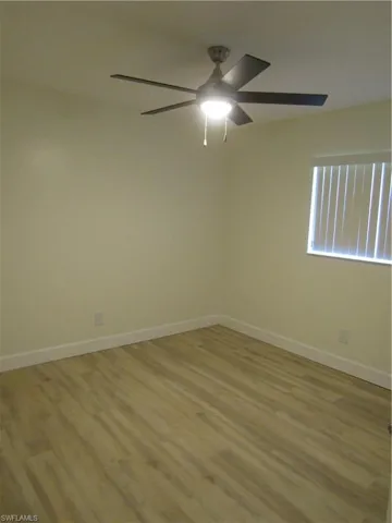 Room featuring light wood-finish flooring, white baseboards, a window with horizontal blinds, and a ceiling fan with integrated lighting