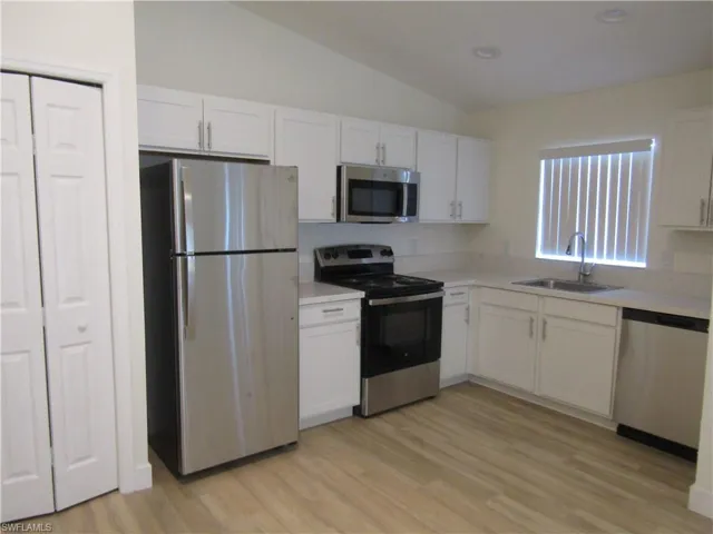 Kitchen featuring stainless steel appliances, white cabinetry, light-toned countertops, wood-finish flooring, and a vaulted ceiling