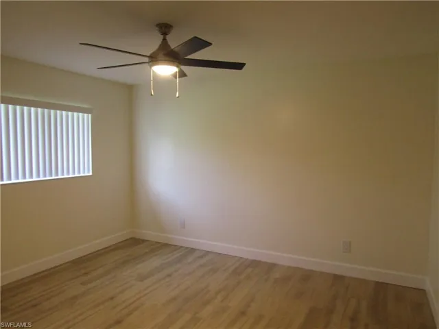Room featuring wood-finish flooring, a ceiling fan with integrated lighting, and a window with vertical blinds