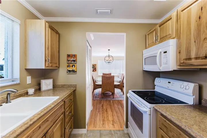 Kitchen with white appliances, crown molding, suspended lighting, and wood finish cabinets