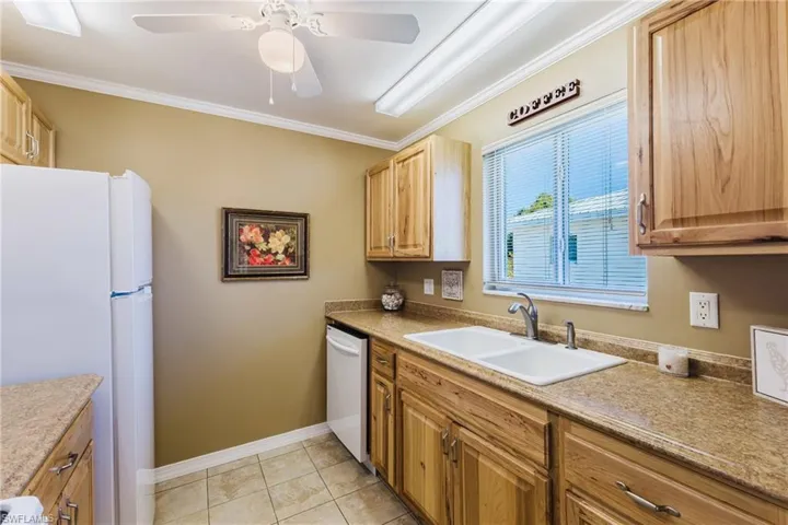 Kitchen featuring white appliances, ornamental molding, ceiling fan, light countertops, and light tile patterned floors