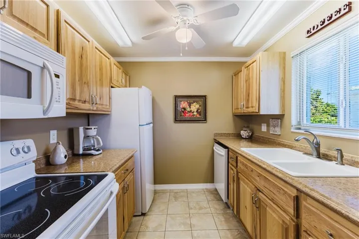 Kitchen featuring white appliances, ornamental molding, ceiling fan, and light tile patterned floors