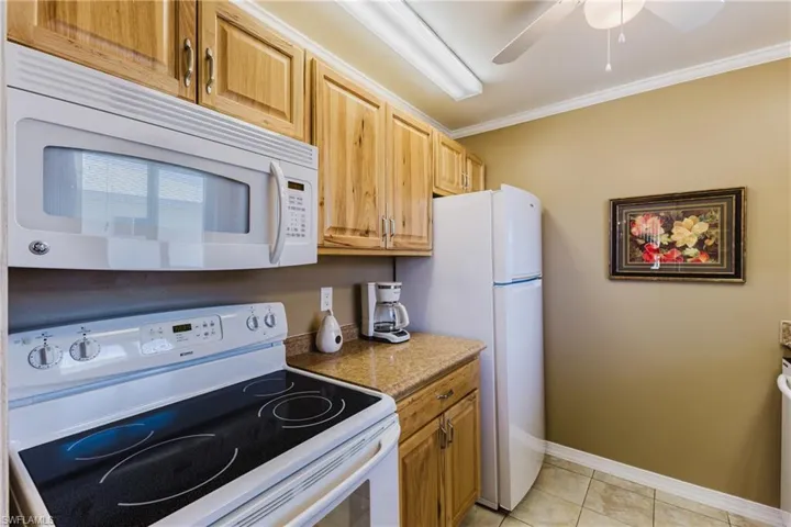Kitchen featuring white appliances, ceiling fan, light stone counters, ornamental molding, and light tile patterned flooring