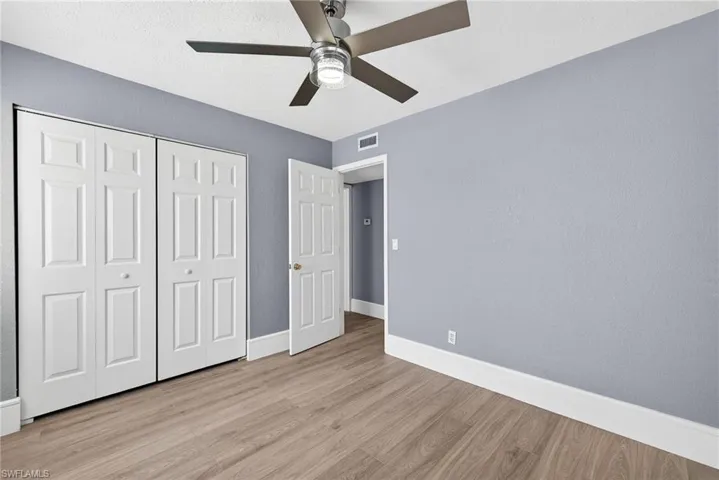 Unfurnished bedroom with light wood-type flooring, a ceiling fan, a closet, and a textured wall