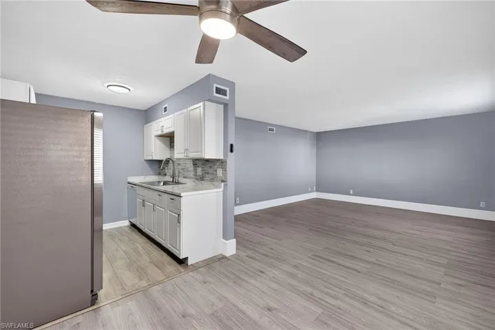 Kitchen with freestanding refrigerator, light countertops, white cabinets, light wood-style flooring, and a ceiling fan