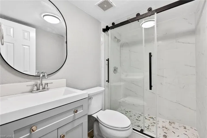 Bathroom featuring a textured wall, vanity, and a marble finish shower