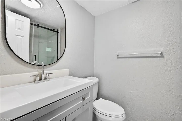 Full bathroom featuring a textured wall, vanity, a marble finish shower, and a textured ceiling