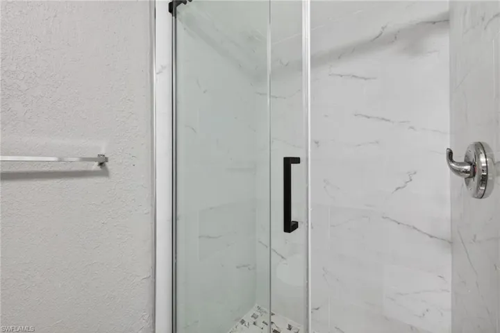Bathroom featuring a marble finish shower and a textured wall