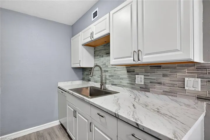 Kitchen with white cabinets, a textured wall, white dishwasher, light wood-style flooring, and backsplash