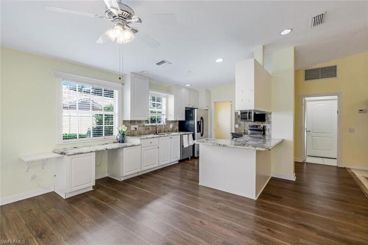 Kitchen with granite countertops, white cabinetry, stainless steel appliances, laminate flooring and a built-in desk area.