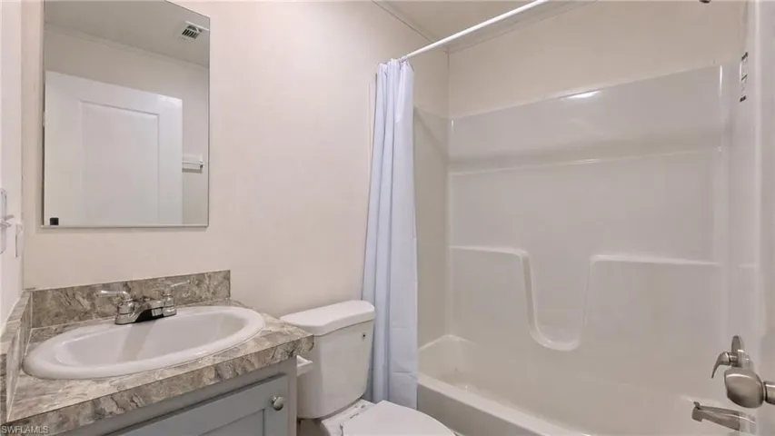 Full bathroom featuring a single vanity with a patterned countertop and white basin, a toilet, and a white tub/shower combination with a shower curtain rod