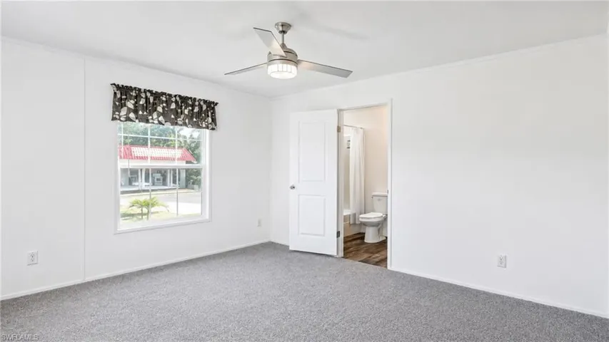 Spacious room featuring gray carpeting, white walls, a ceiling fan with integrated lighting, and a window with a valance